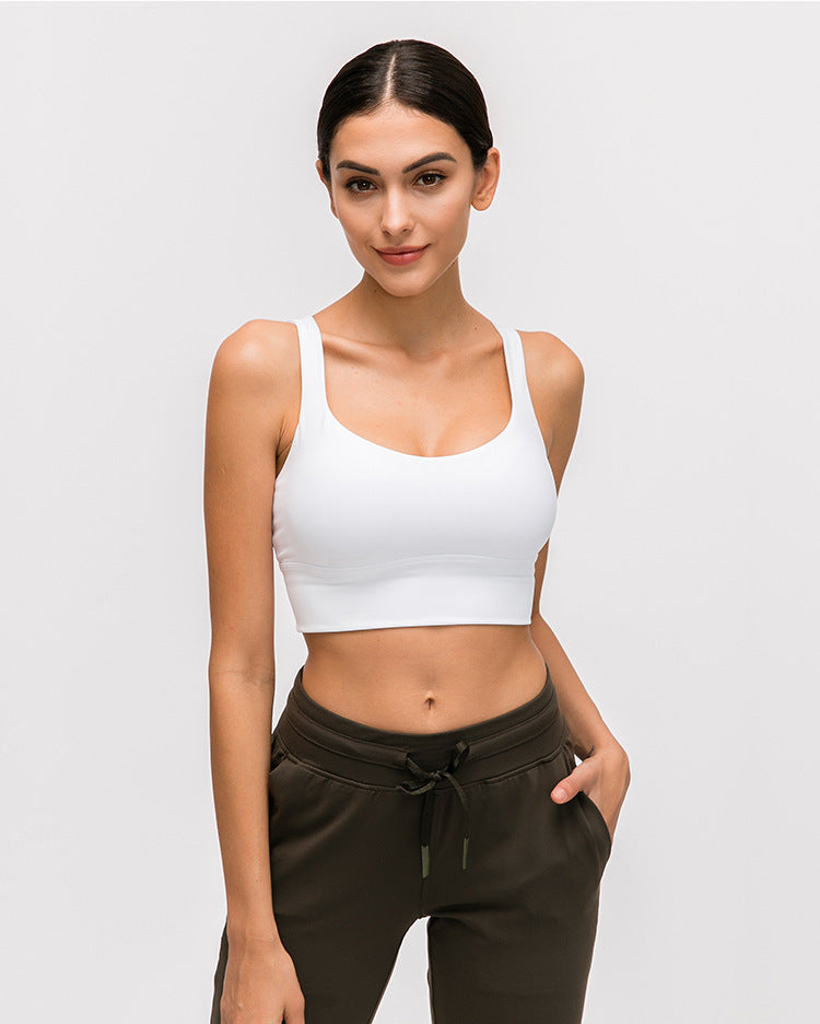 Woman wearing a white sports bra and brown pants on a light gray background