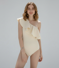 Woman wearing a beige one-shoulder dress against a plain background