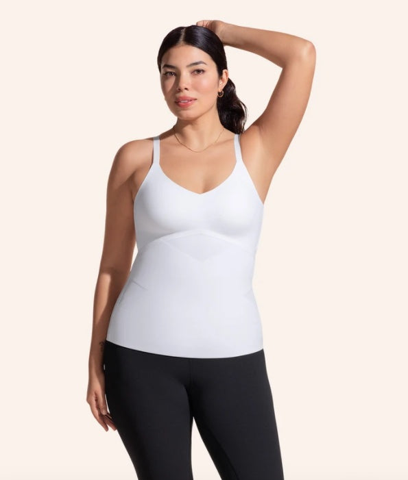 Woman wearing a white tank top and black leggings on a beige background