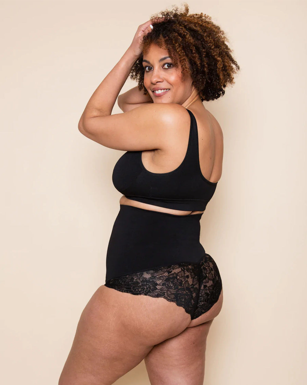 Woman wearing a black lace lingerie set against a beige background