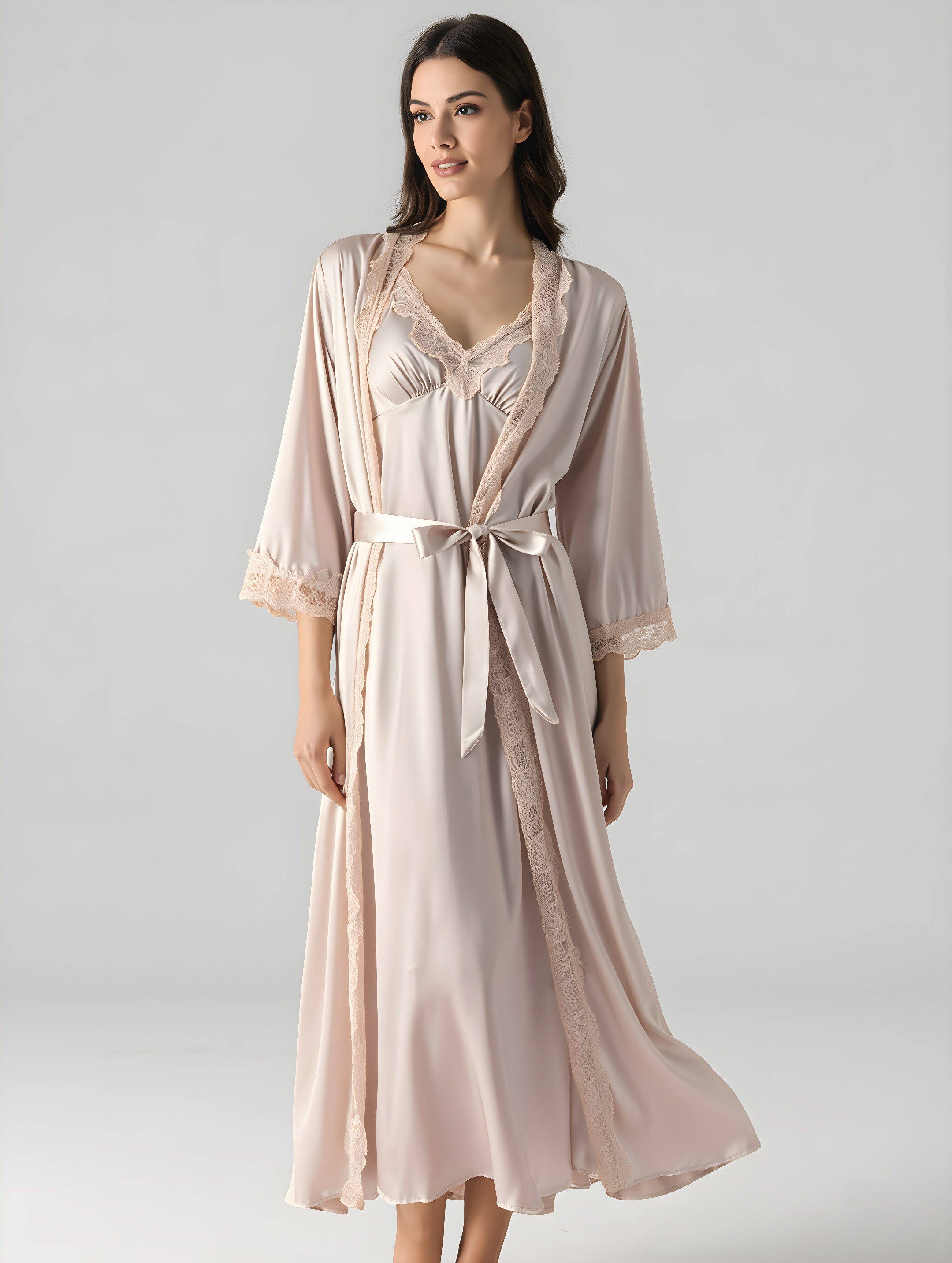 Woman wearing a light pink satin nightgown with a matching robe on a plain background
