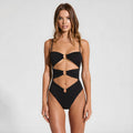 Woman wearing a black swimsuit with cut-out design on a light gray background