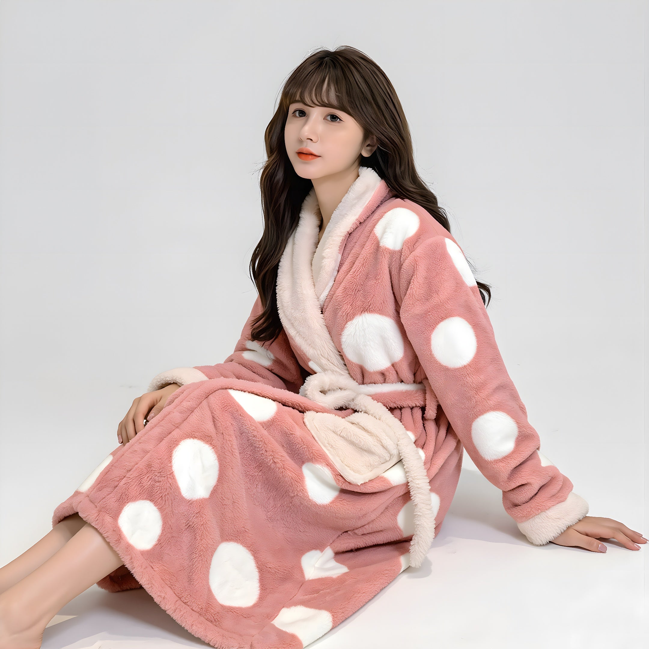 Woman wearing a pink robe with white polka dots on a plain background